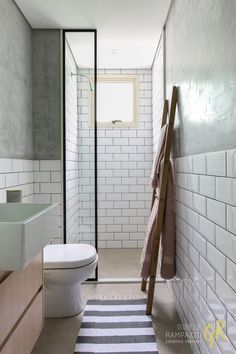 a white toilet sitting next to a bathroom sink under a window in a tiled wall