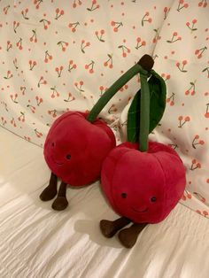 two stuffed cherries sitting on top of a bed next to each other with leaves