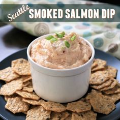 a black plate topped with crackers and a bowl of smoked salmon dip surrounded by chips