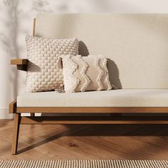 three pillows sitting on top of a wooden bench in front of a white wall and wood floor