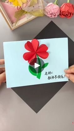 someone is holding up a card with flowers on it and writing in the chinese language