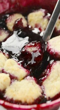 blueberry cobbler in a red bowl with ice cream on the rim and spoon