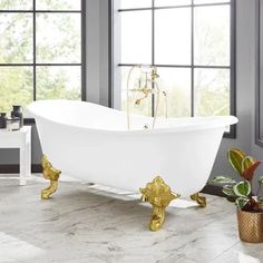 a white bath tub sitting in a bathroom next to two potted plants and windows