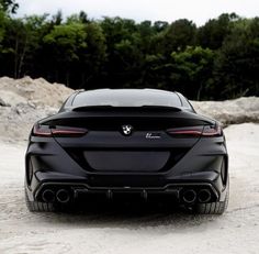 the rear end of a black sports car parked in front of some rocks and trees