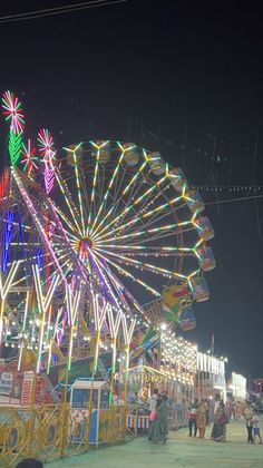 a ferris wheel lit up at night with people walking around the carnival area in the background