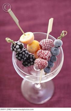 a glass filled with fruit on top of a purple table next to a pink wall