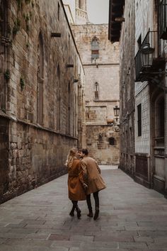 two people walking down an alley way in the middle of town, one holding the other's hand