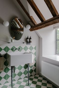 a bathroom with green and white tiles on the floor, sink and window in the corner