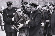 black and white photograph of men in uniform walking down the street, one holding an accordion