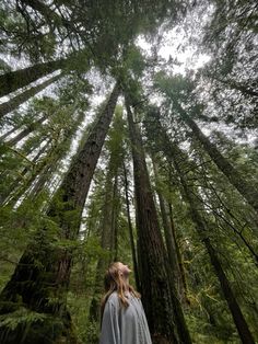 a woman standing in the middle of a forest looking up into the sky with her eyes closed