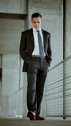 a man wearing a suit and tie standing in front of a building with his hands in his pockets