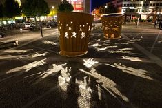 two large trash cans sitting on the side of a road at night with people walking by