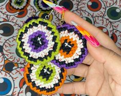 a hand holding two crocheted earrings in front of a colorful background with circles