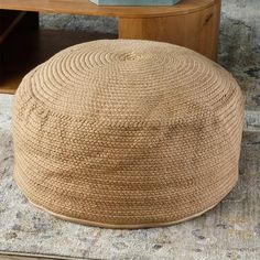 a large round ottoman sitting on top of a rug next to a wooden table and shelf