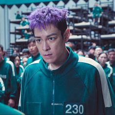 a young man with purple hair standing in front of a group of people wearing green jackets