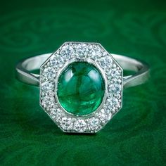 an emerald and diamond ring sitting on top of a green cloth covered table with diamonds around it