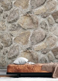 a brown leather bench sitting in front of a stone wall with a blanket on it