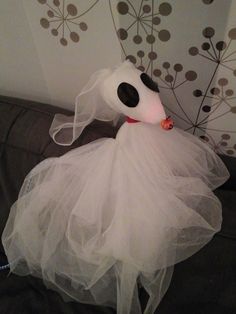 a stuffed dog dressed up in a white dress and veil sitting on top of a couch