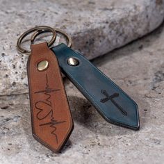 two leather keychains with the words jesus and a cross on them sitting on a rock