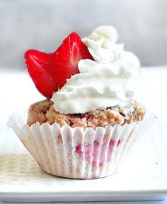 a white plate topped with a cupcake covered in whipped cream and a strawberry on top