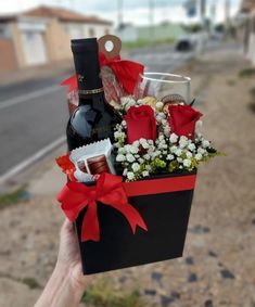 a person holding a wine bottle and flowers in a gift box on the side of a road