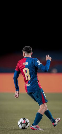 a man in blue and red uniform kicking a soccer ball on the field at night