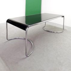 a black table with a green chair on it's back end in front of a white wall