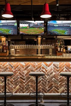 three bar stools in front of a brick wall with two televisions on it