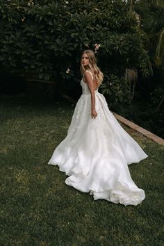 a woman standing in the grass wearing a wedding dress