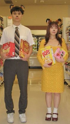 two people standing in a grocery store holding snacks and cereals, one is wearing a cat costume