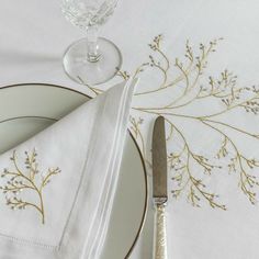 a table setting with white linens and gold trim, silverware and napkins