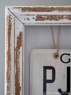 an old wooden sign hanging on the side of a white painted frame with rope attached to it