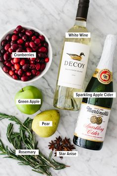 ingredients to make cranberry apple cider recipe on marble counter top with wine bottle, pears and rosemary