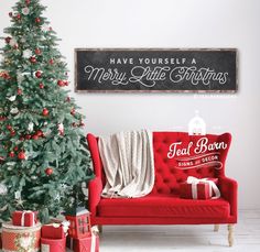 a red couch sitting next to a christmas tree in front of a sign that says have yourself a merry little christmas