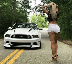 a woman standing next to a white mustang