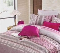 a bed covered in pink and white comforter next to a window