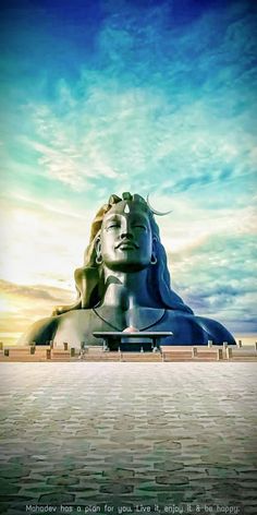 a large statue sitting in the middle of a brick floored area under a cloudy blue sky