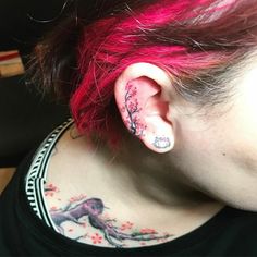 a woman with red hair has tattoos on her neck and behind her ear, which is an image of a bird