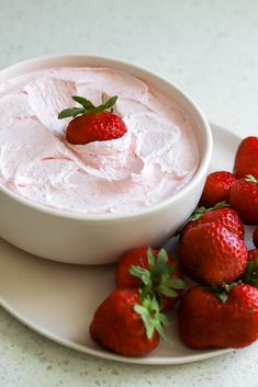 some strawberries are on a plate next to a bowl of dip