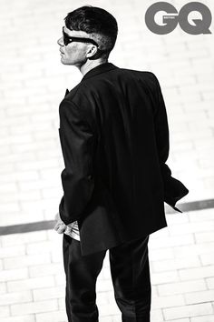 a man in a suit and sunglasses standing on the street with his back to the camera