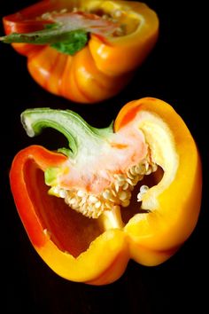 two bell peppers cut in half on a black surface with one pepper still attached to the other