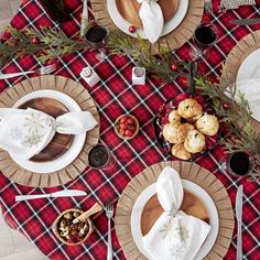 the table is set for christmas dinner with red and black checkered linens, white plates, silverware