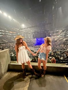 two women in short shorts and cowboy hats holding hands while standing on the edge of an arena