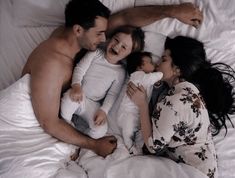 a group of people laying on top of a bed next to each other with one woman holding a baby