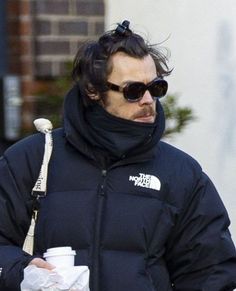 a man in a black jacket and sunglasses holding a coffee cup while walking down the street