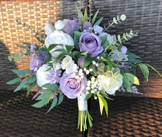 a bridal bouquet with purple flowers and greenery on a wicker tablecloth