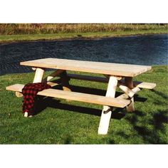 a wooden picnic table sitting on top of a lush green field next to a river