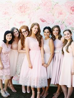 a group of women standing next to each other in front of a wall with flowers on it