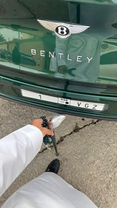 a person holding scissors in front of a bentley car