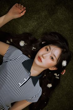 a young woman laying on the ground with her hand up to her head and flowers in her hair